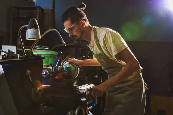 Concentrated male manufacture worker in protective apron and goggles using machine tool at factory — Stock Photo