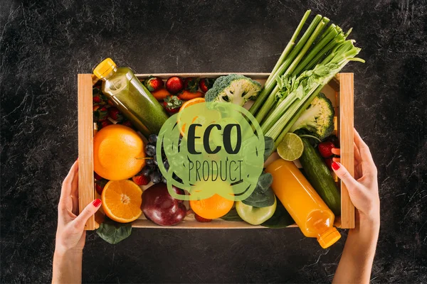 Partial view of woman holding wooden box with healthy vegetables, fruits and detox drinks with 