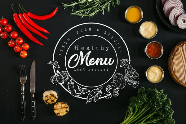 Top view of various sauces, grilled garlic, fork with knife and fresh vegetables with herbs on black background with 