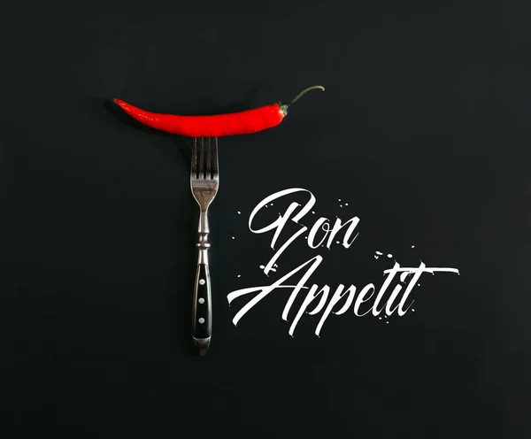 Piment rouge à la fourchette sur fond noir avec inscription 