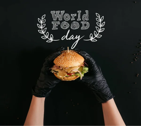 Recortado tiro de manos en guantes sosteniendo deliciosa hamburguesa con pavo, verduras y aderezo César en negro con letras 