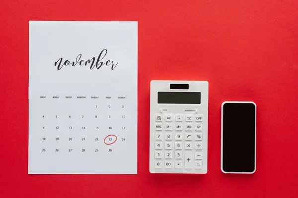 Top view of calendar for November, calculator and smartphone isolated on red, black friday concept — Stock Photo