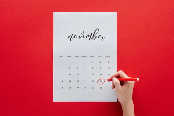 Visão parcial da mulher escrevendo sexta-feira preta no calendário para novembro isolado no vermelho — Fotografia de Stock