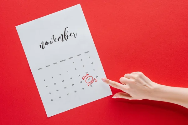 Recortado vista de la mujer señalando viernes negro en el calendario para noviembre aislado en rojo - foto de stock