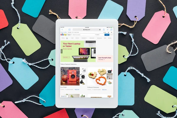 Top view of digital tablet with ebay website on screen lying on colorful sale tags — Stock Photo