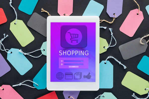 Top view of digital tablet with shopping app on screen lying on colorful sale tags — Stock Photo