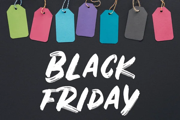 Vue de dessus des étiquettes de vente colorées sur fond noir avec lettrage noir vendredi — Photo de stock