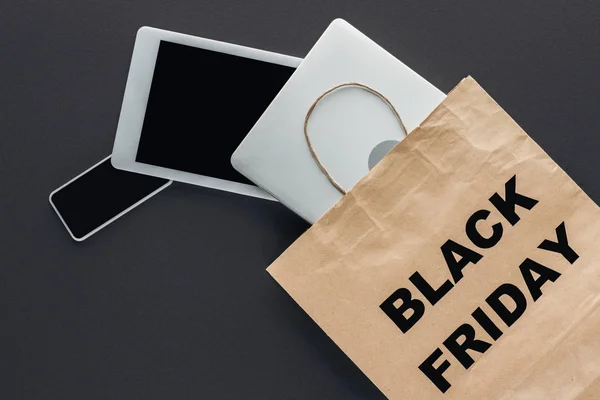 Top view of digital devices in shopping bag with black friday symbol on black — Stock Photo