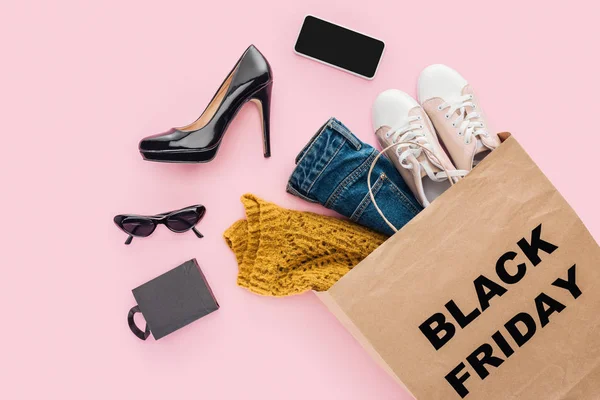 Acostado plano con ropa en bolsa de compras con signo de viernes negro aislado en rosa - foto de stock