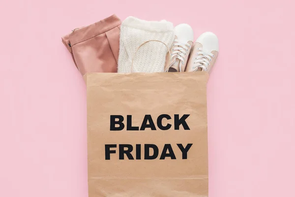 Top view of stylish clothes in shopping bag with black friday sign isolated on pink — Stock Photo