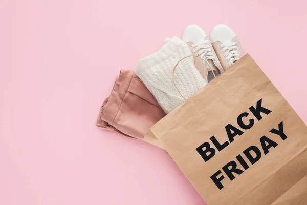 Vista dall'alto dei vestiti nella shopping bag con simbolo del venerdì nero isolato sul rosa — Foto stock