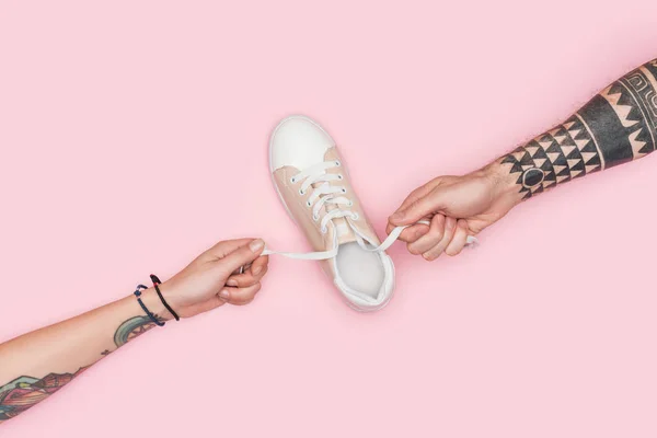 Частичный вид татуированных людей, держащих шнурки кроссовок изолированы на розовый — стоковое фото
