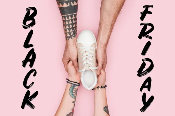 Cropped view of tattooed shopaholics holding sneaker isolated on pink with black friday lettering — Stock Photo