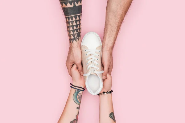 Cropped view of tattooed couple holding one sneaker isolated on pink — Stock Photo
