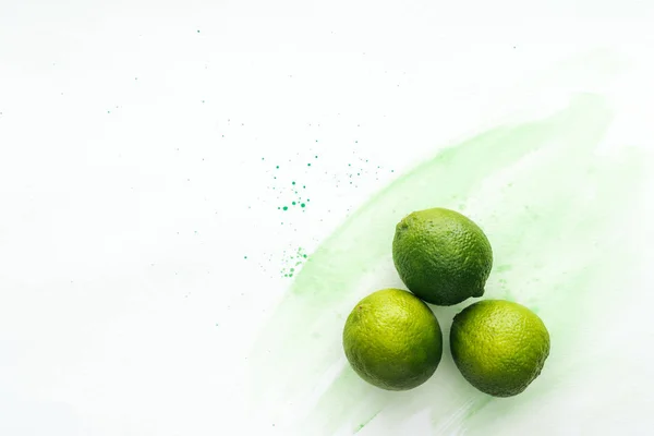 Vue de dessus de trois chaux mûres sur la surface blanche avec aquarelle verte — Photo de stock