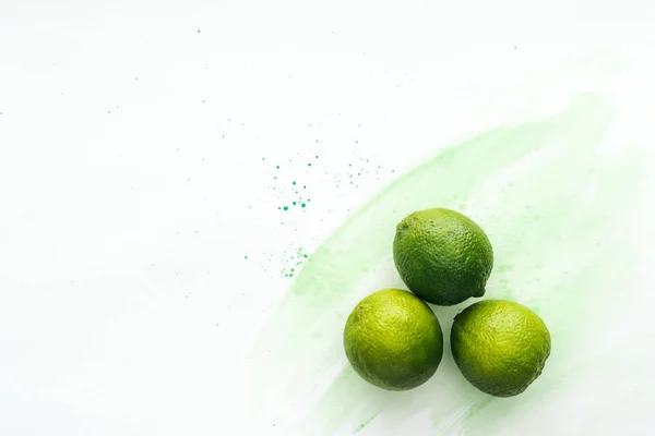 Top view of three ripe limes on white surface with green watercolor — Stock Photo
