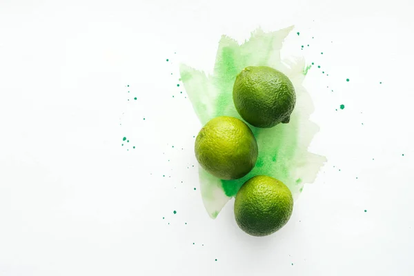 Draufsicht auf ganze drei reife Limetten auf weißer Oberfläche mit grünem Aquarell — Stockfoto