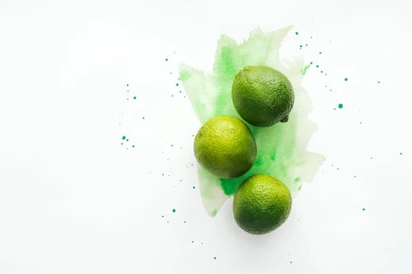 Top view of whole three ripe limes on white surface with green watercolor — Stock Photo