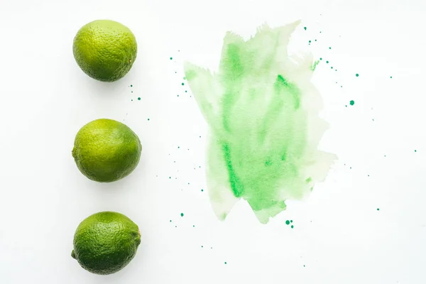 Верхний вид спелых лаймов в ряд на белой поверхности с зеленой акварелью — стоковое фото