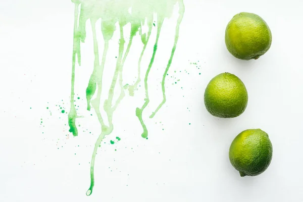 Повышенный вид цельных лаймов на белой поверхности с зеленой акварелью — стоковое фото