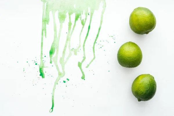 Elevated view of whole limes on white surface with green watercolor — Stock Photo