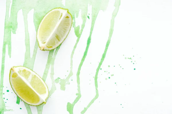 Draufsicht auf zwei Stücke reife Limetten auf weißer Oberfläche mit grünem Aquarell — Stockfoto