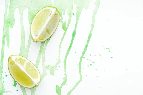 Top view of two pieces of ripe limes on white surface with green watercolor — Stock Photo