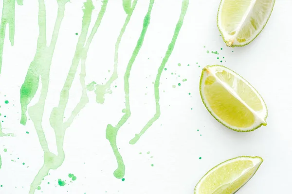 Vue de dessus de trois morceaux de limes mûres sur la surface blanche avec aquarelle verte — Photo de stock
