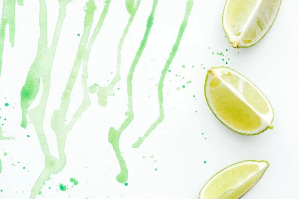 Top view of three pieces of ripe limes on white surface with green watercolor — Stock Photo