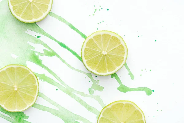 Vue de dessus des limes coupées sur la surface blanche avec aquarelle verte — Photo de stock