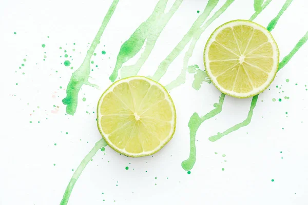 Vue surélevée de deux morceaux de limes mûres sur surface blanche avec aquarelle verte — Photo de stock