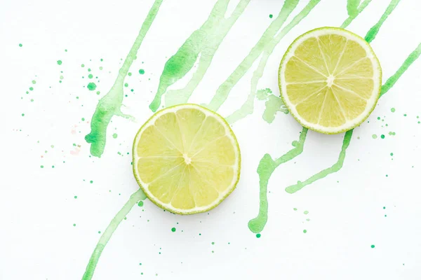 Elevated view of two pieces of ripe limes on white surface with green watercolor — Stock Photo