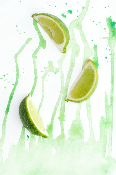 Top view of pieces of organic limes on white surface with green watercolor — Stock Photo
