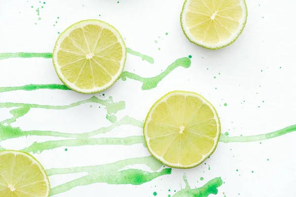 Top view of pieces of cut ripe limes on white surface with green watercolor — Stock Photo