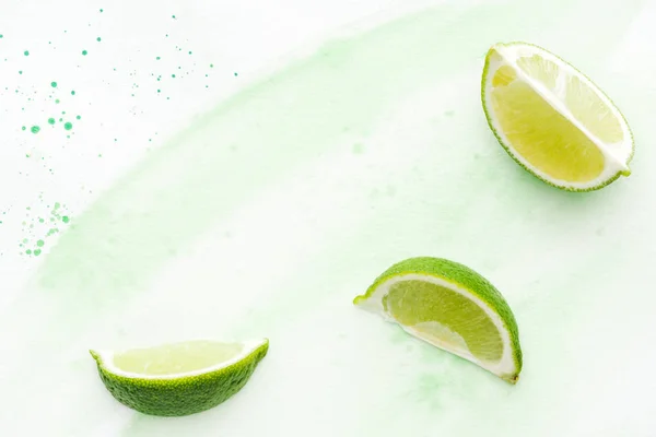 Draufsicht auf Stücke von leckeren Limetten auf weißer Oberfläche mit grüner Aquarellfarbe — Stockfoto