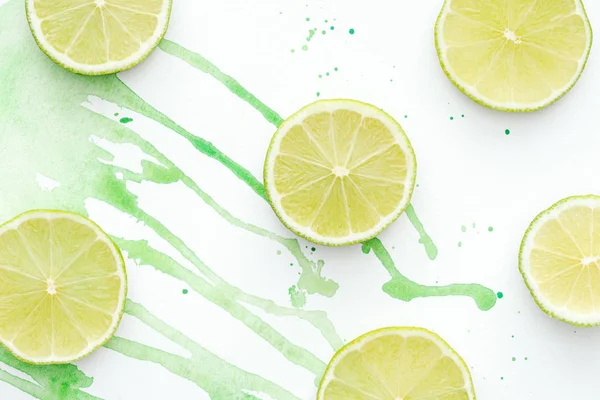 Top view of pieces of ripe raw limes on white surface with green watercolor — Stock Photo