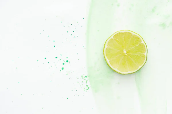 Elevated view of piece of ripe lime on white surface with green watercolor — Stock Photo