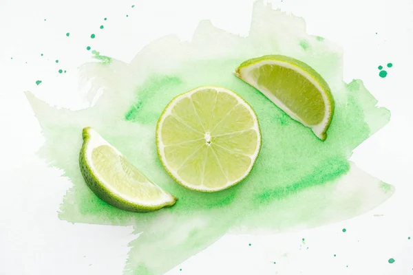 Vista superior de pedaços de limas verdes maduras na superfície branca com aquarela verde — Fotografia de Stock