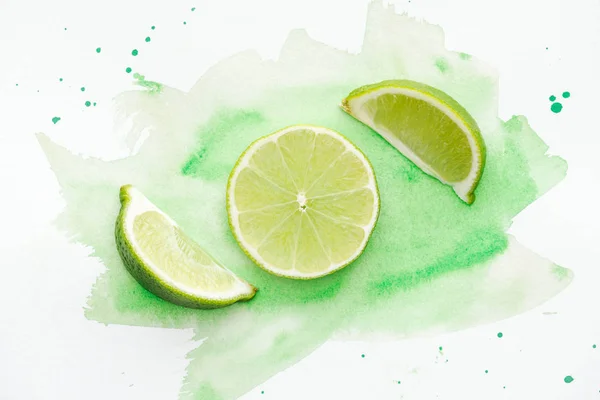 Top view of pieces of green ripe limes on white surface with green watercolor — Stock Photo