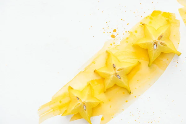 Draufsicht auf drei exotische Sternfrüchte auf weißer Oberfläche mit gelbem Aquarell — Stockfoto