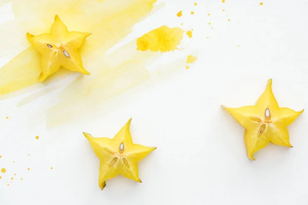 Vista superior de tres frutos estelares maduros en superficie blanca con acuarela amarilla - foto de stock