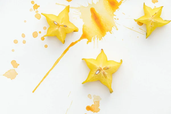 Vue de dessus de trois fruits étoilés sur surface blanche avec éclaboussures de peinture jaune — Photo de stock