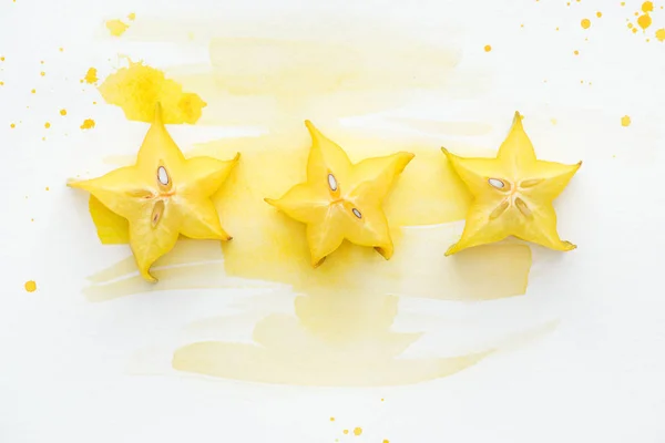 Vue du dessus des fruits étoilés en rangée sur la surface blanche avec aquarelle jaune — Photo de stock