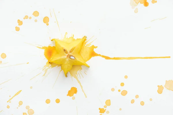 Vista elevada de la fruta estrella amarilla en la superficie blanca con salpicaduras de pintura amarilla - foto de stock