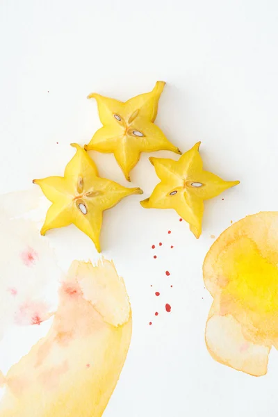 Vista superior de las frutas estrella en la superficie blanca con acuarela amarilla - foto de stock