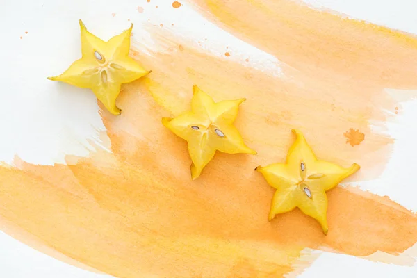 Draufsicht auf süße exotische Sternfrüchte auf weißer Oberfläche mit orangefarbenem Aquarell — Stockfoto