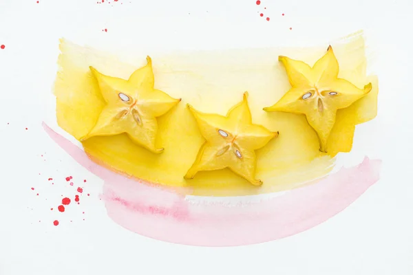 Top view of three ripe star fruits on white surface with yellow and pink watercolors — Stock Photo