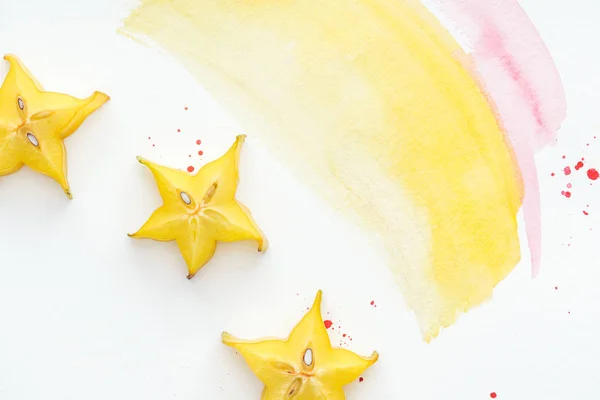 Top view of yummy carambolas on white surface with yellow and pink watercolors — Stock Photo