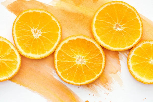 Вид сверху на апельсиновые кусочки на белой поверхности с оранжевой акварелью — стоковое фото