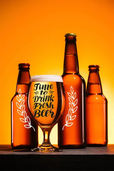 Bottles and glass of beer with foam on surface on orange background with 